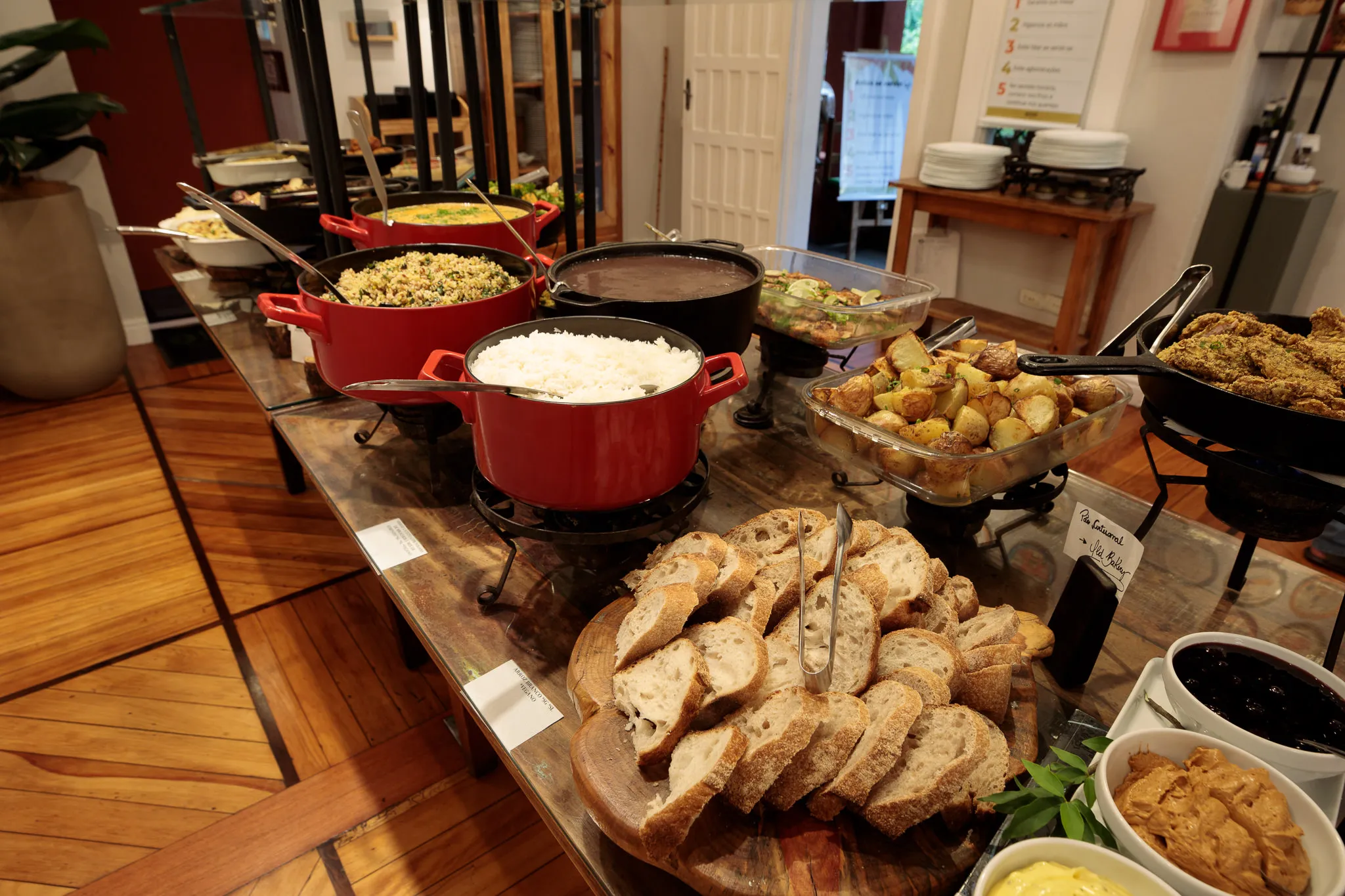 Mesa gastronômica do Quintana com pães, arroz, saladas e pratos quentes em panelas coloridas